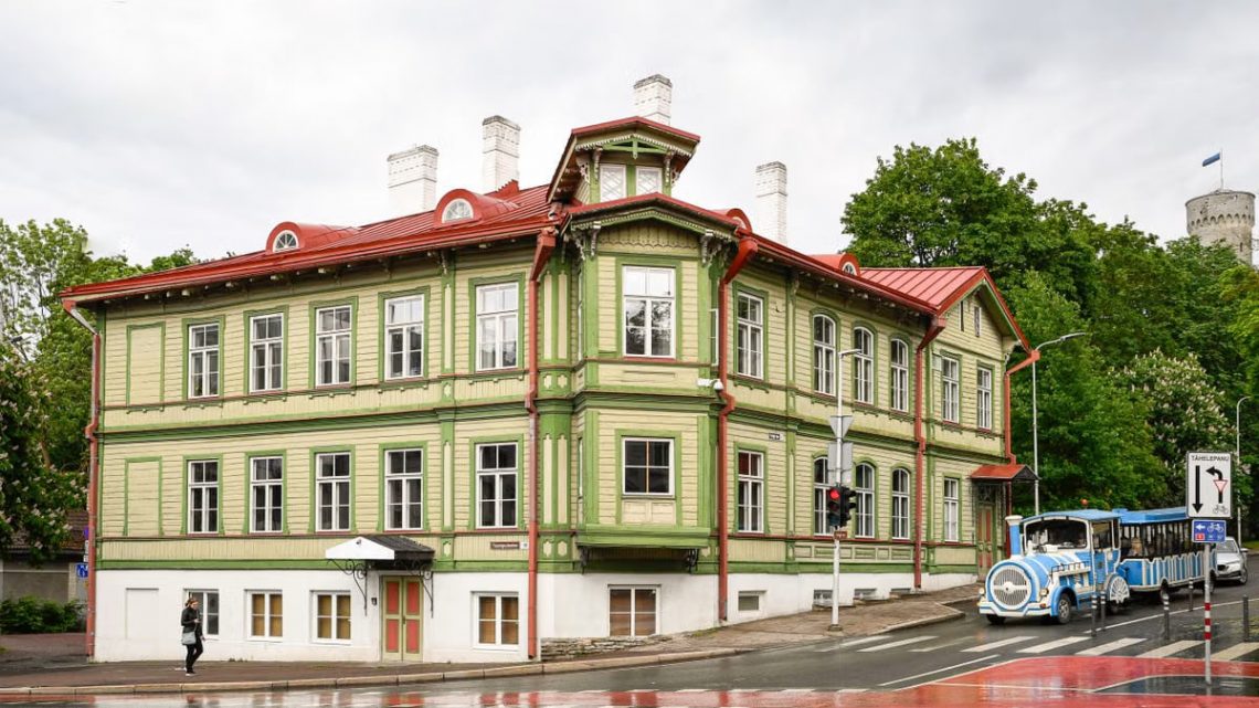 Charming green facade wooden building on a rainy day in Tallinn's Kassisaba, featuring urban life and tourist attractions.