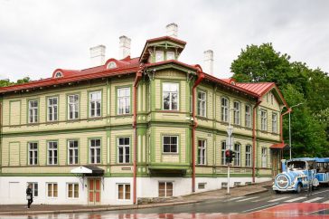 Charming green facade wooden building on a rainy day in Tallinn's Kassisaba, featuring urban life and tourist attractions.