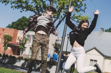 Two teenagers joyfully jumping outdoors in Šiluva, Lithuania under a bright blue sky. Captured in springtime.